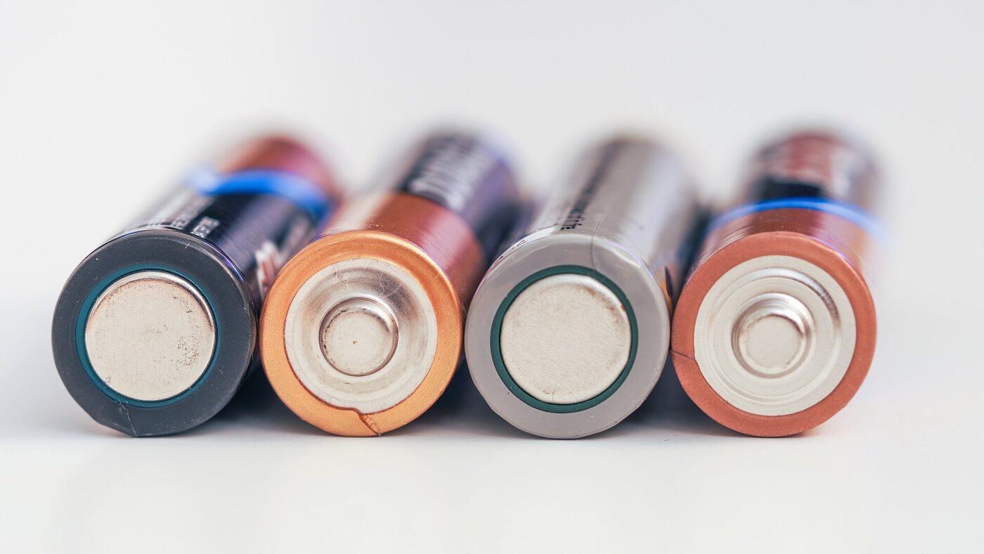 A close-up of four AA batteries lined up with their flat ends forward.