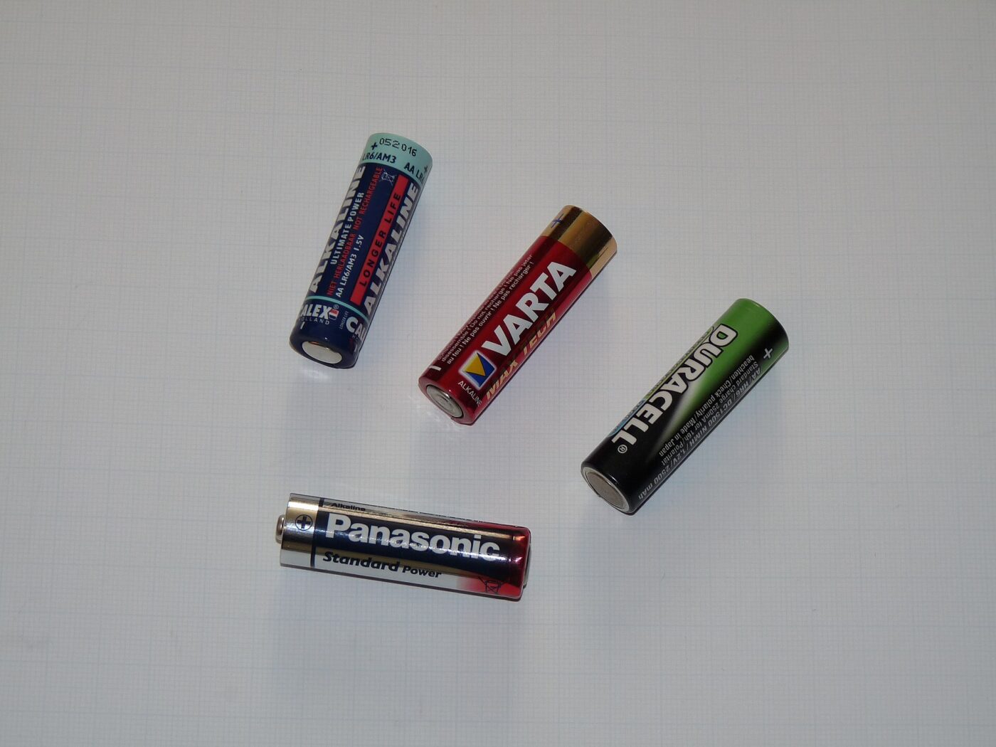 Four AA batteries from different brands lying on a plain grey surface.