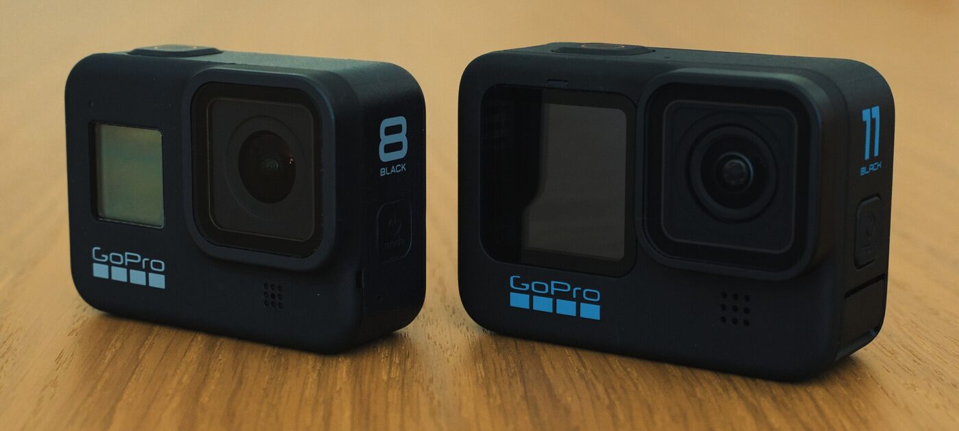 Two GoPro action cameras, a Hero 8 Black and a Hero 11 Black, on a wooden table