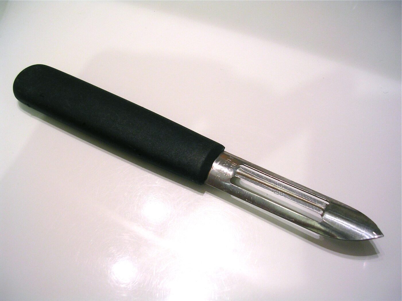 A straight vegetable peeler with a thick, soft rubber handle on a white surface.