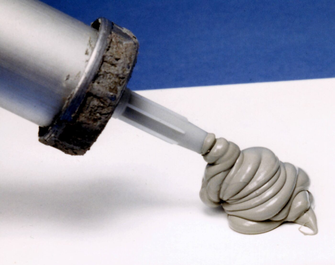 Grey sealant squeezed from a caulking gun nozzle into a soft coil