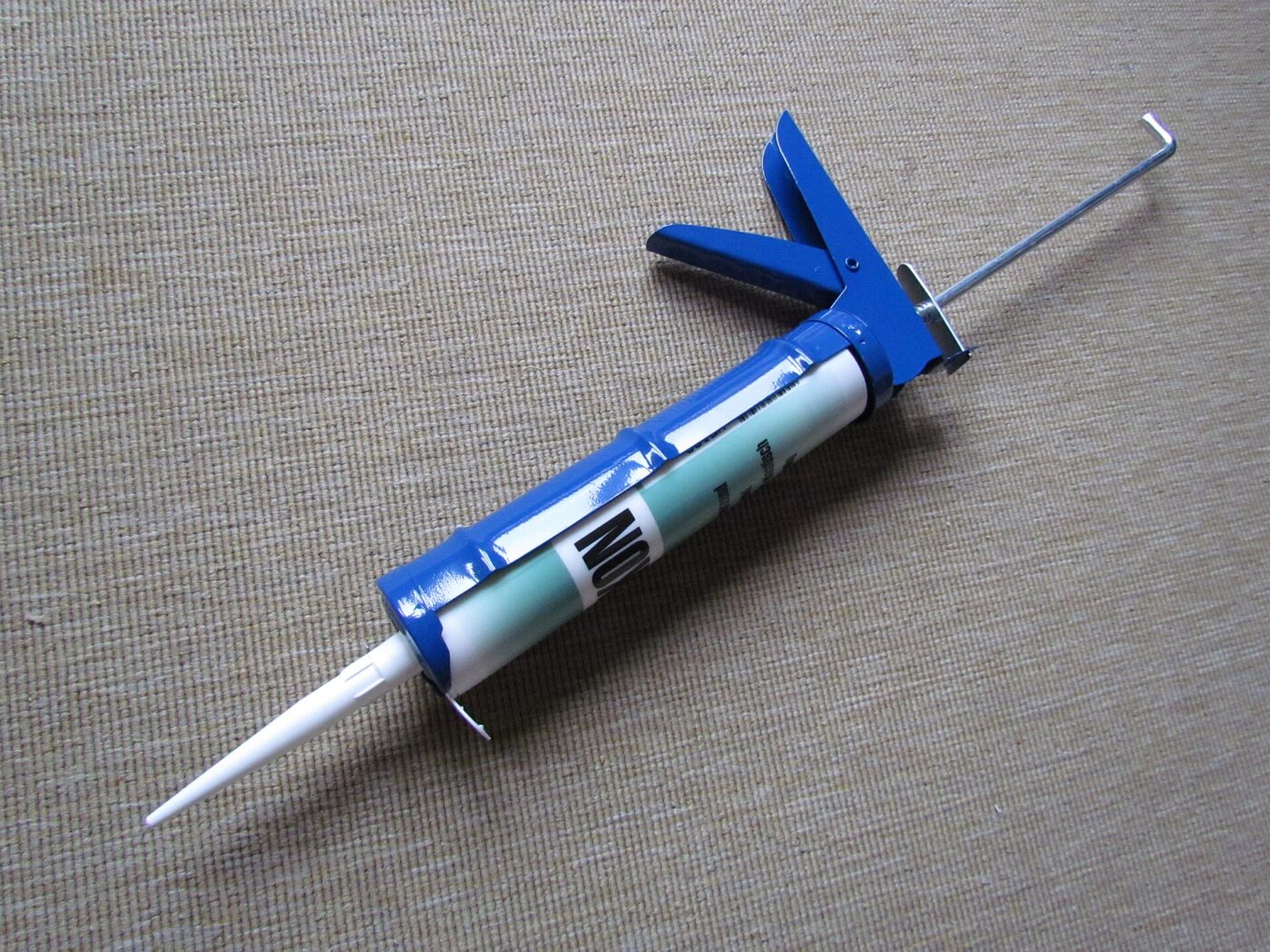 A skeleton caulking gun loaded with a sealant cartridge, lying on a grey floor