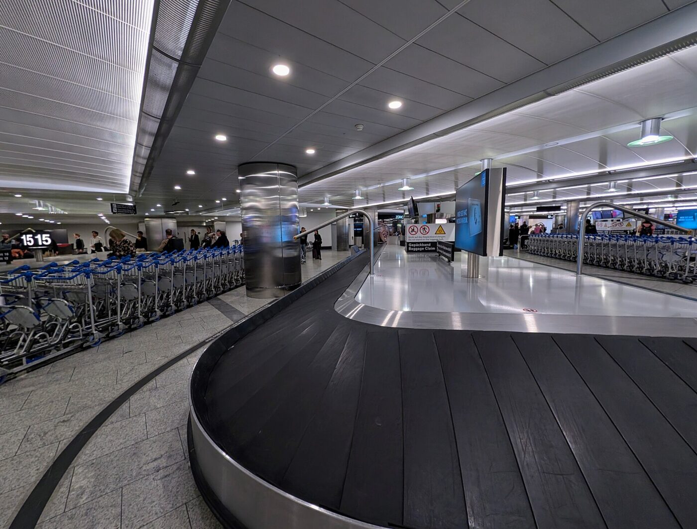 An empty airport baggage claim belt beside long rows of luggage carts
