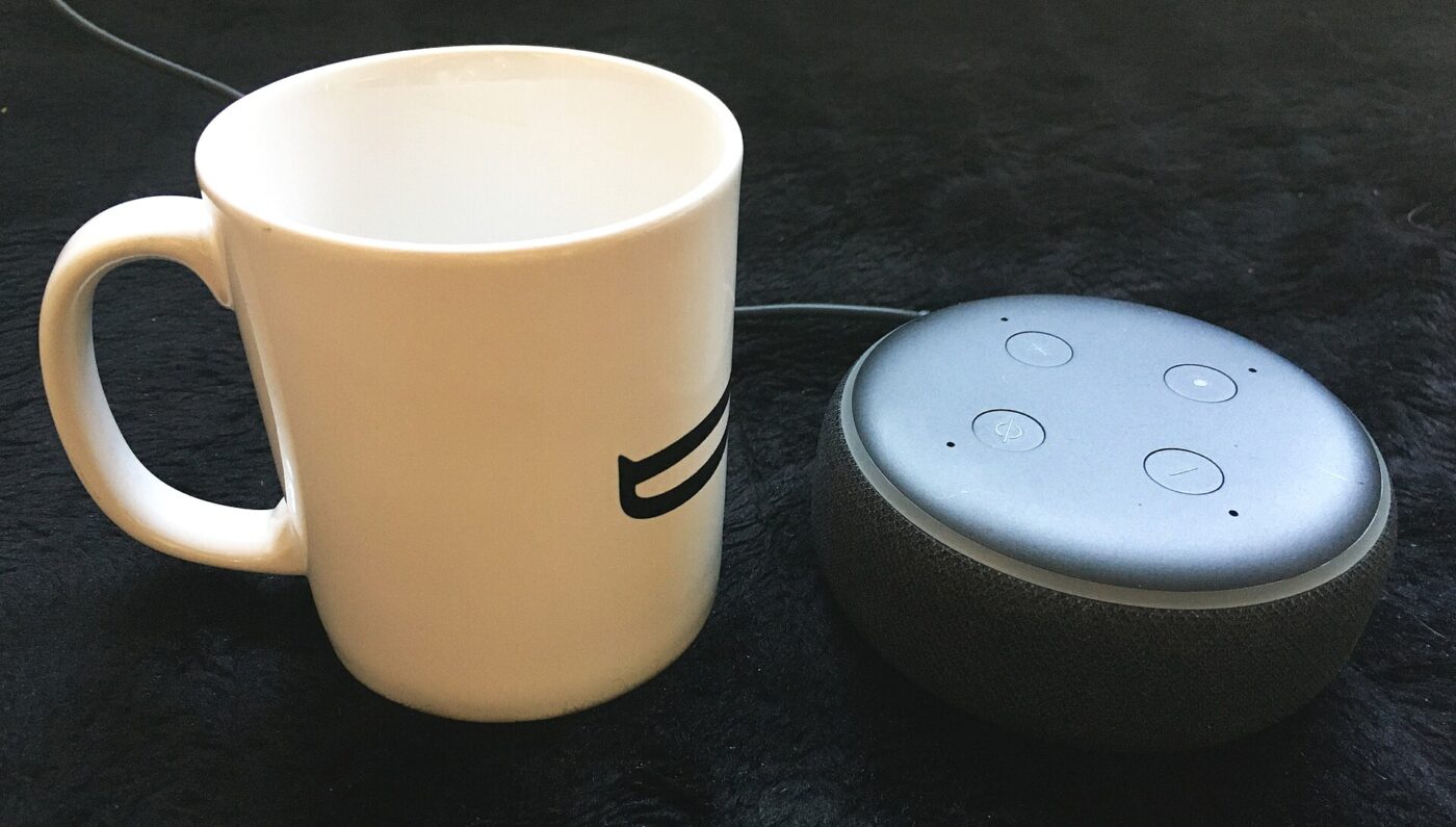 A small round smart speaker next to a white coffee mug for a sense of scale