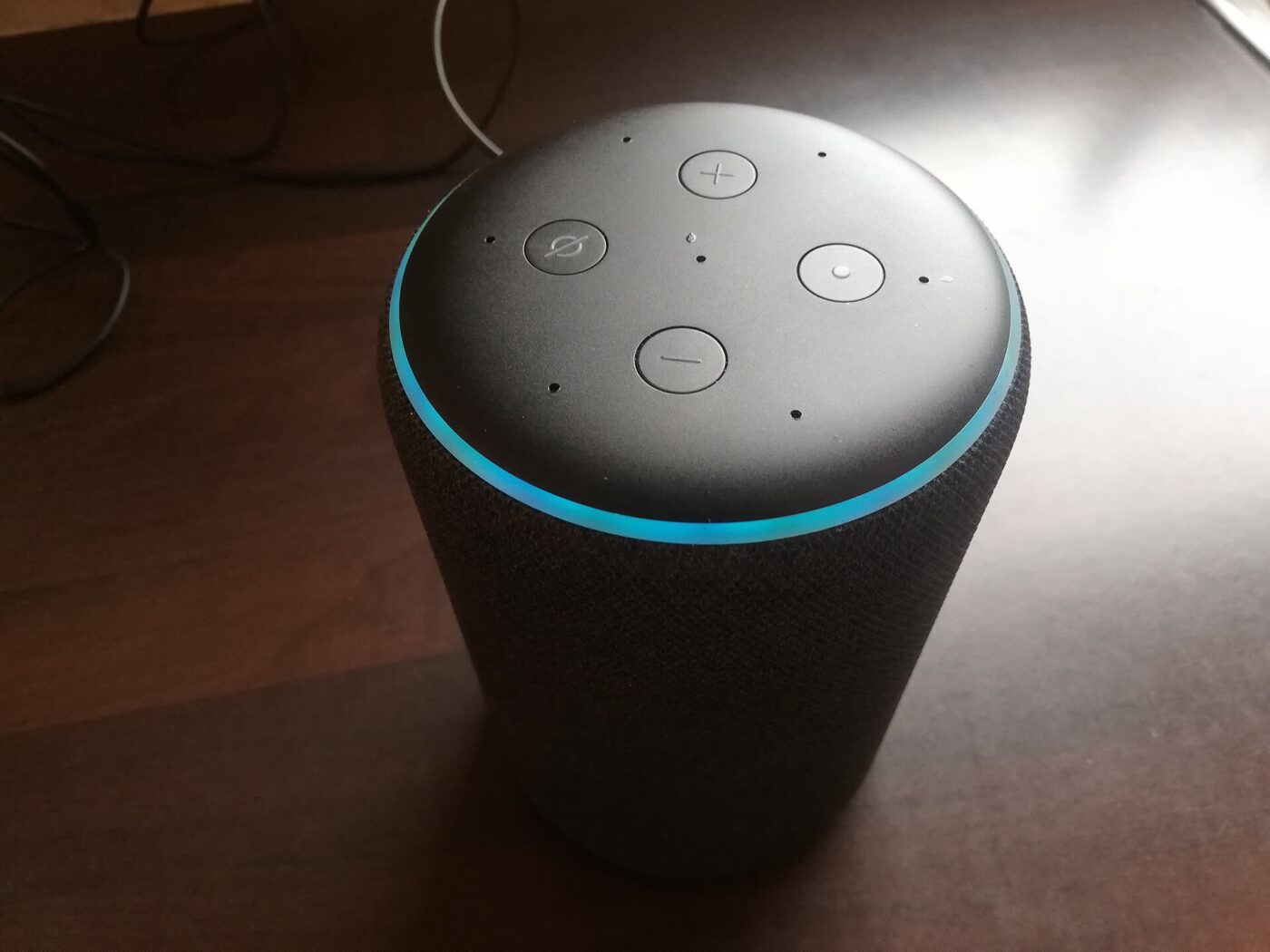 A fabric-covered smart speaker with a glowing blue light ring sitting on a wooden table