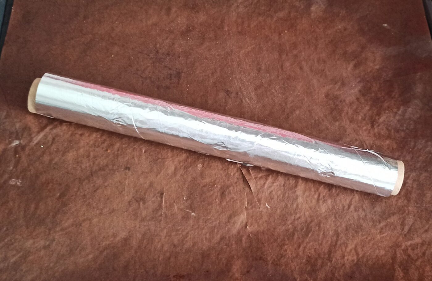 A roll of kitchen foil lying on a sheet of brown baking paper.