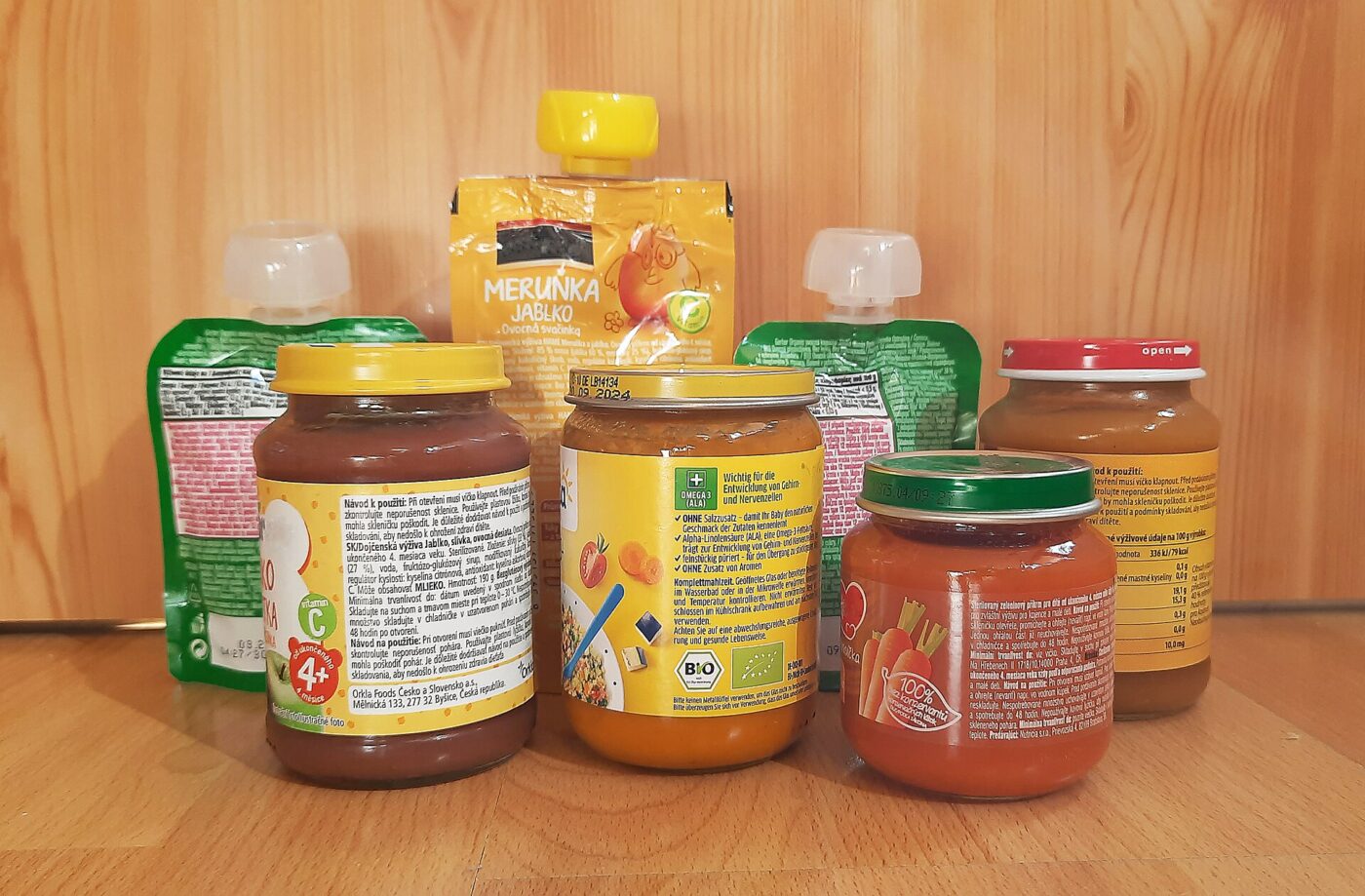 Jars and squeeze pouches of store-bought fruit and vegetable baby food on a wooden shelf