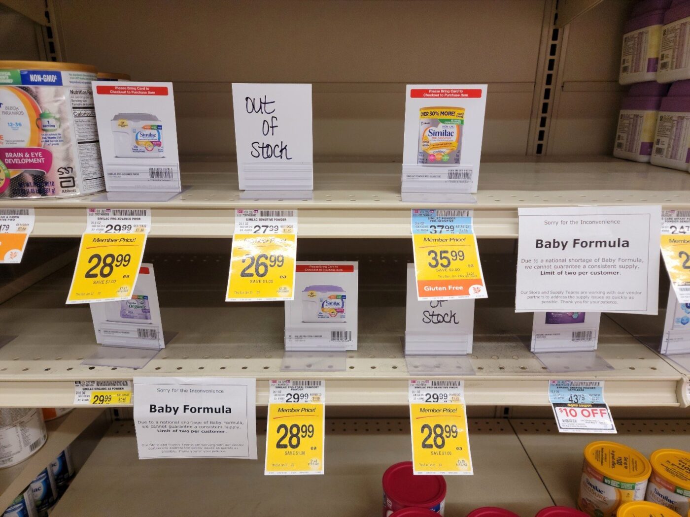 Store shelf of baby formula with yellow price tags, out-of-stock signs and a purchase limit notice