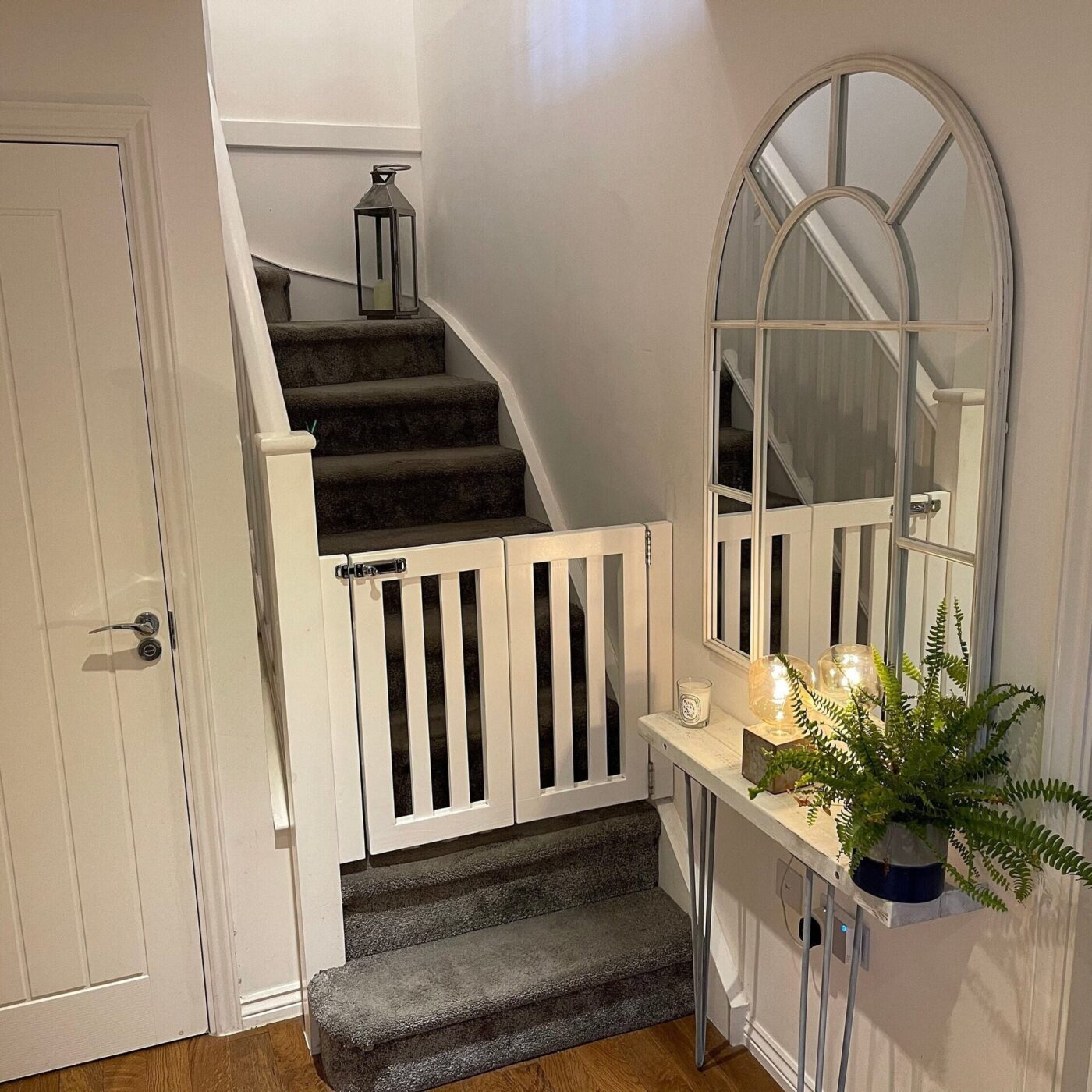 A white wooden safety gate fitted across the bottom of a carpeted staircase.
