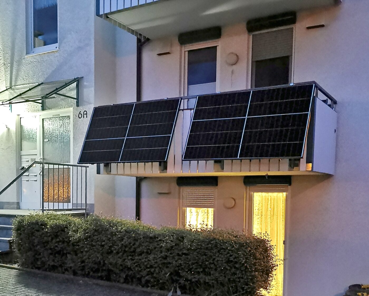 Two solar panels mounted on the railing of a small balcony of a residential building at dusk