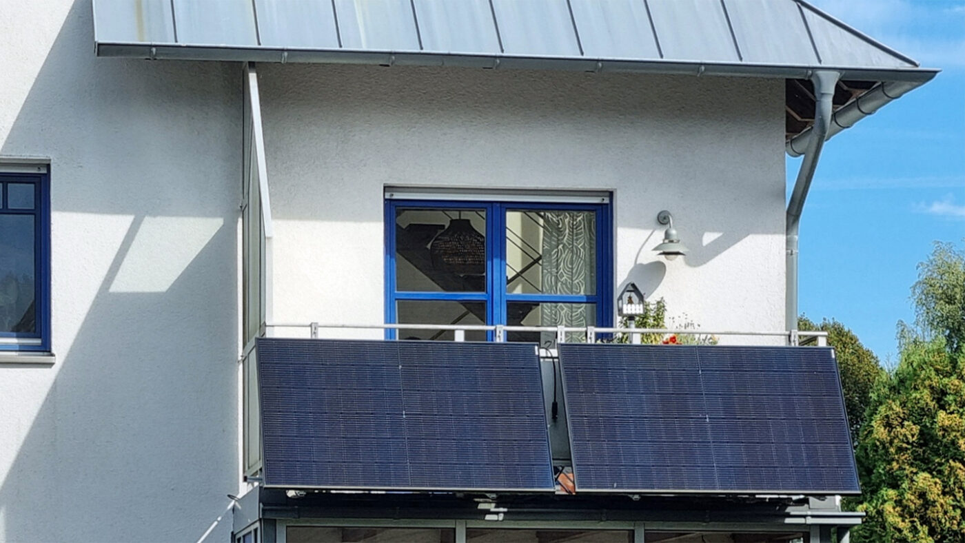 Two solar panels hung on the railing of a sunny balcony below a window and metal roof