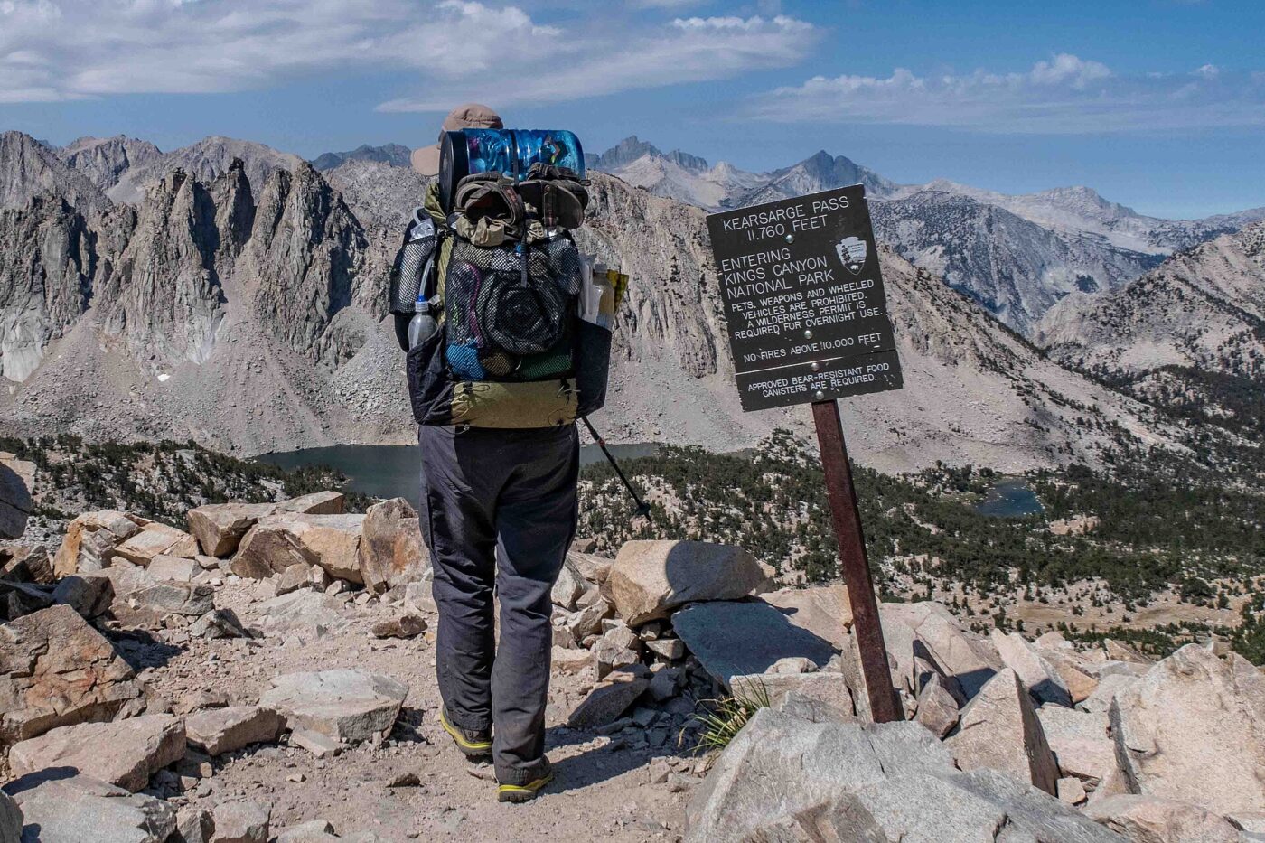 A backpacker with a full pack stops at a trail sign on a high mountain pass