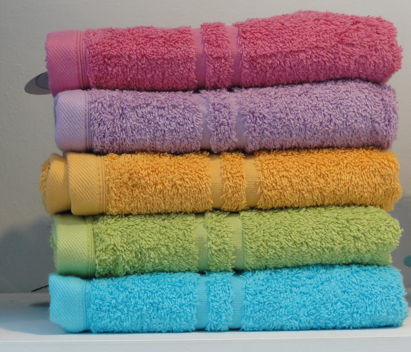 A stack of five folded towels in pink, purple, yellow, green and blue.