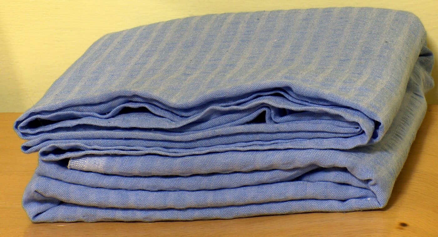 A folded stack of blue woven bed sheets resting on a wooden table.