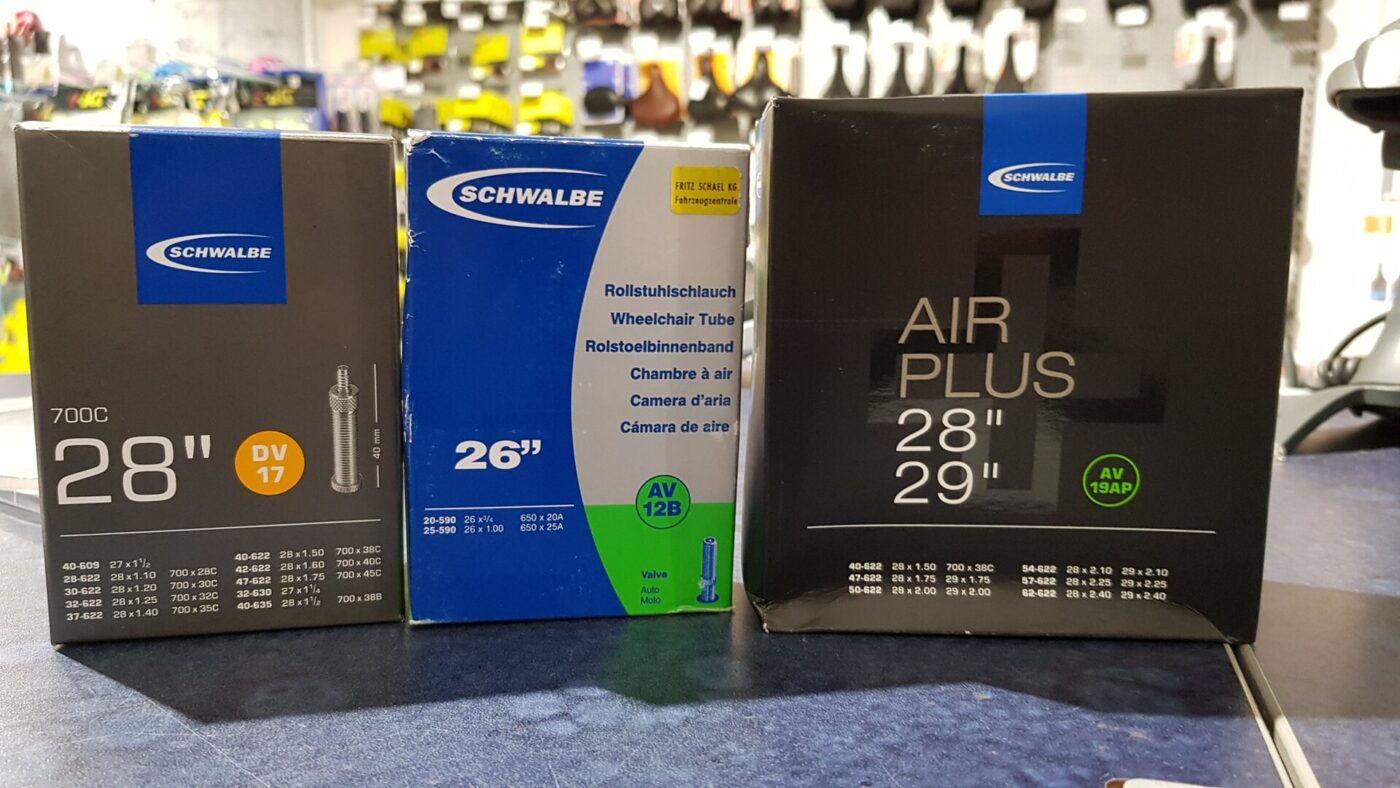 Three boxed bicycle inner tubes in different wheel sizes stand on a shop counter.