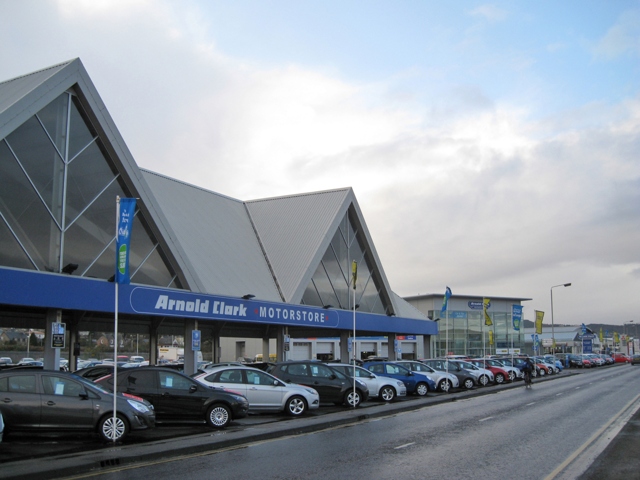 Cars lined up for sale outside a large used car dealership on a gray day