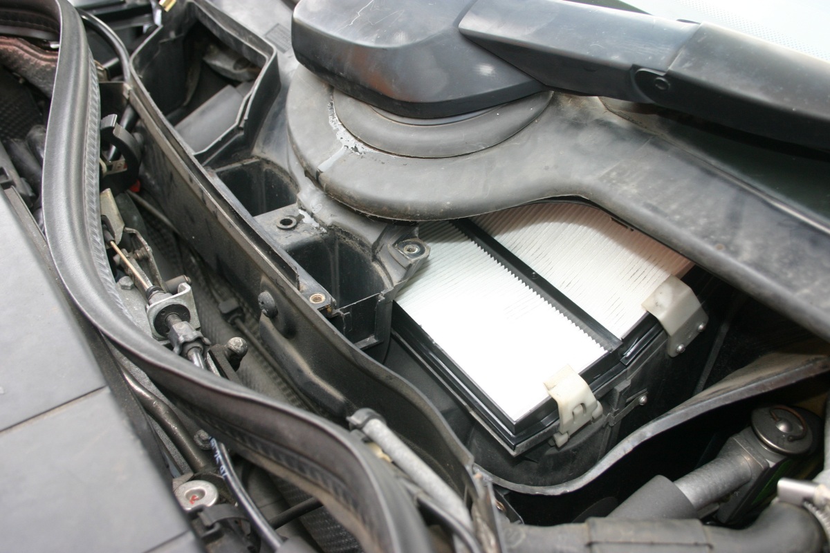 A cabin air filter element sitting in its open housing inside a car's engine bay