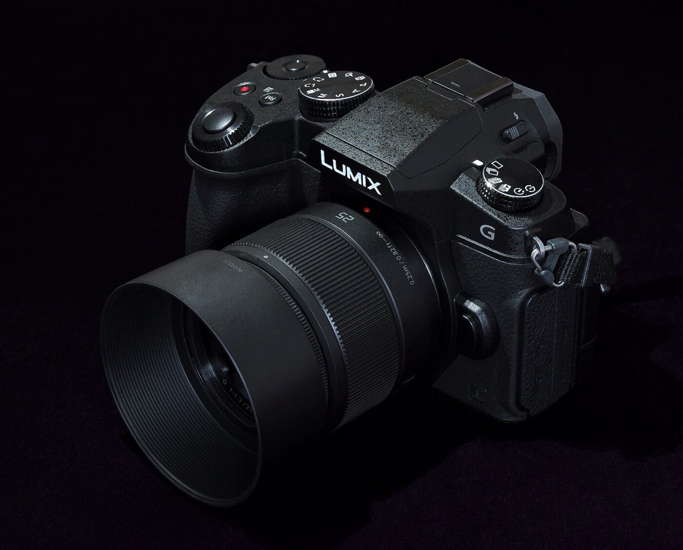 A Panasonic Lumix mirrorless camera fitted with a lens and lens hood against a black background