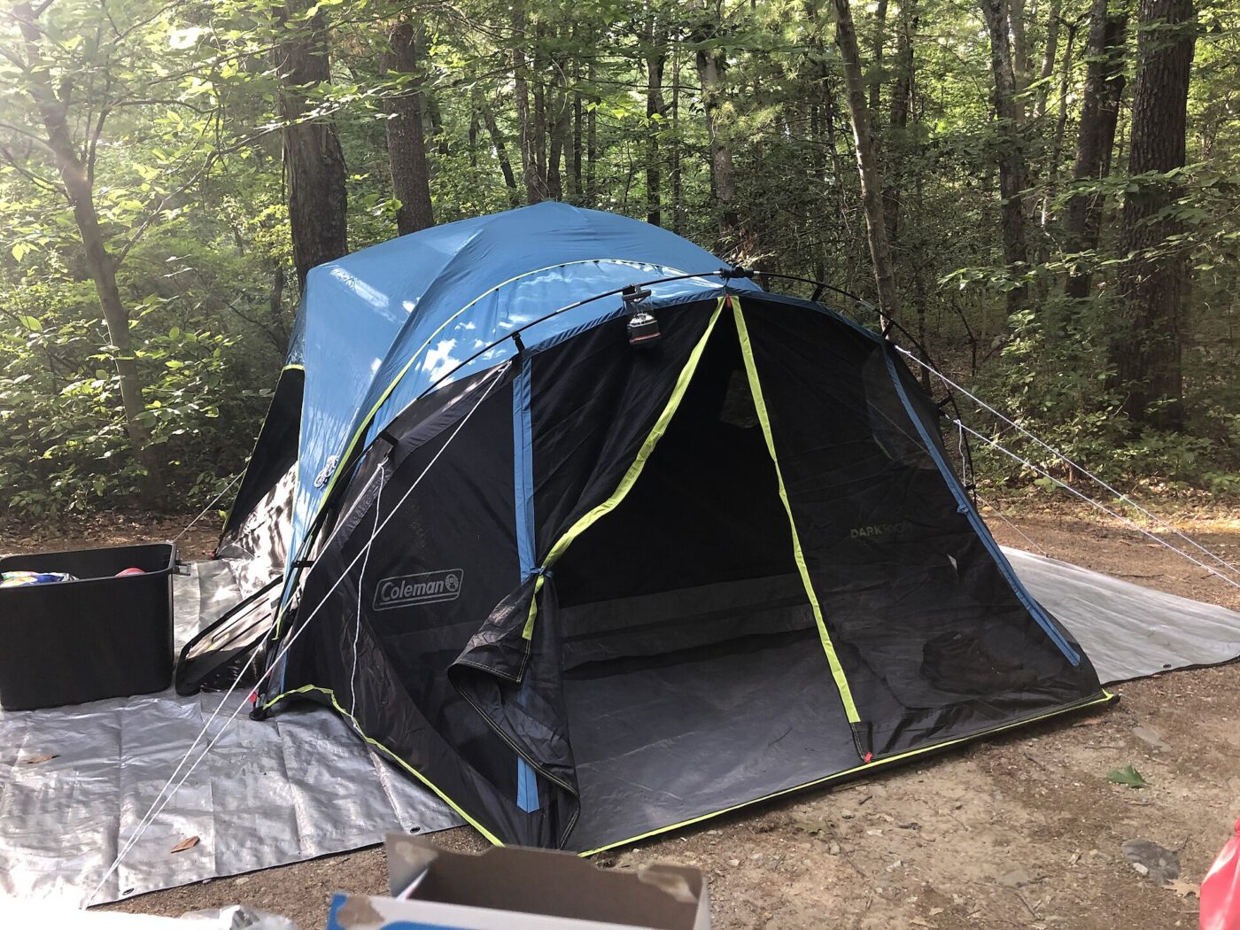 A blue dome tent pitched on a ground tarp at a wooded campsite