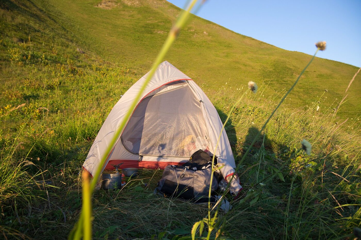 A small backpacking tent pitched on a grassy mountain slope in low golden sunlight