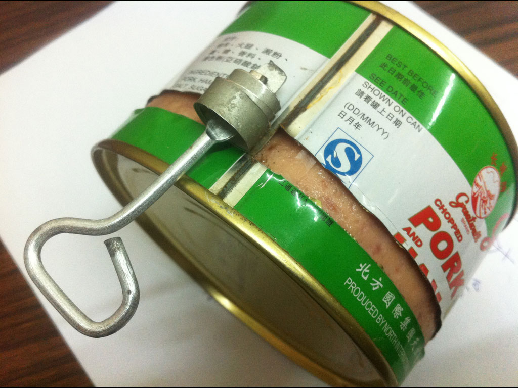 A steel meat can lying on its side with a metal key opener attached to the lid