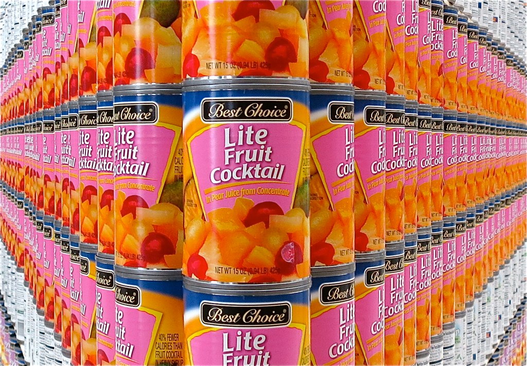 Rows of canned fruit cocktail stacked several cans deep on a supermarket shelf