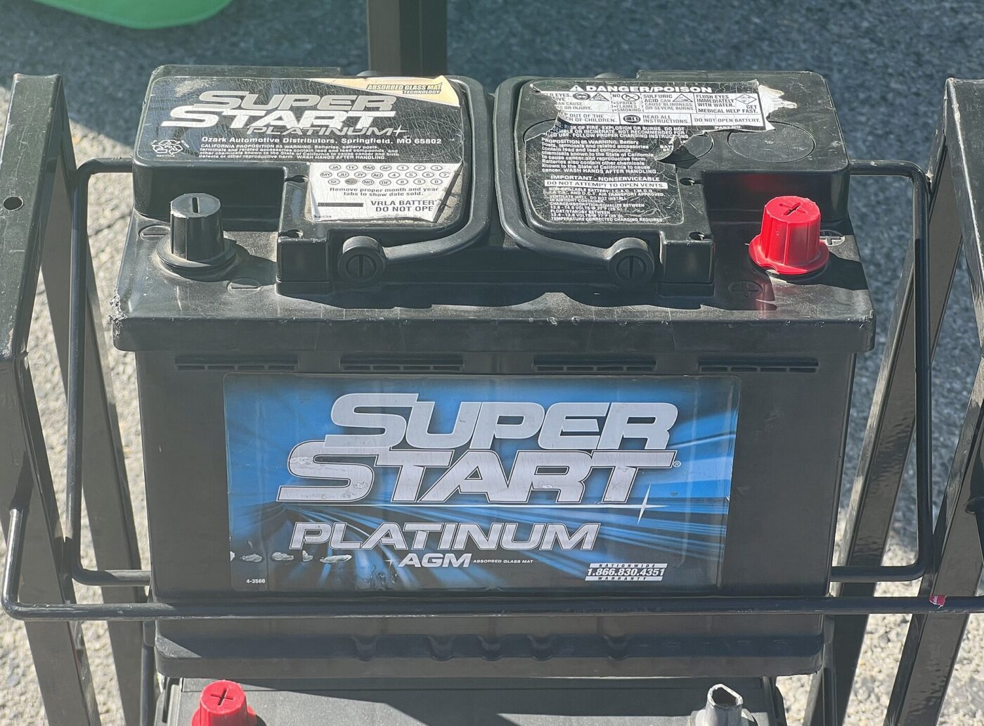 A replacement car battery marked AGM sitting in a metal rack