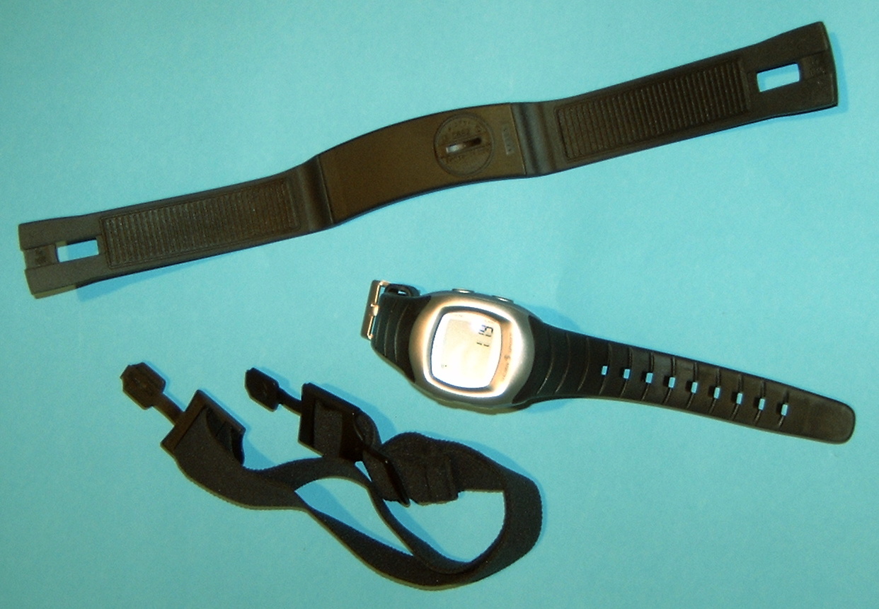 A heart rate chest strap and its elastic belt beside the watch that receives the signal.