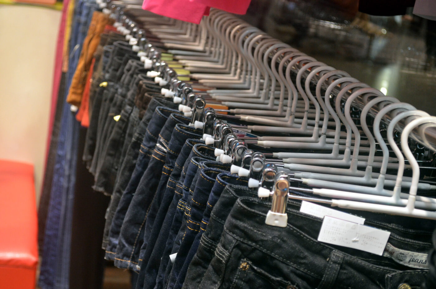 Jeans hanging on white plastic hangers along a rack in a clothing store