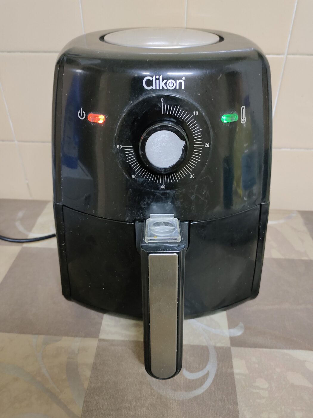 A small black air fryer with a dial timer sitting on a tiled kitchen counter.
