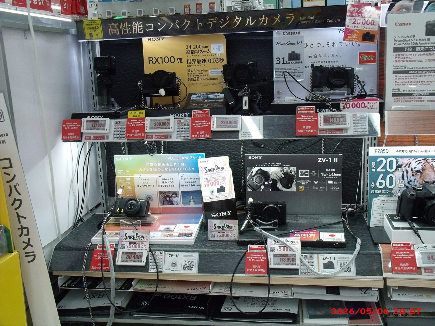 Compact digital cameras on a store display shelf with price tags and Japanese signage