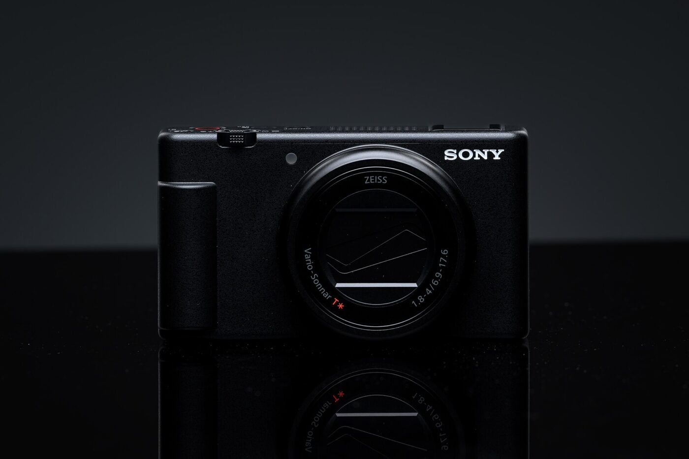 A black Sony compact camera with a Zeiss zoom lens on a reflective black surface