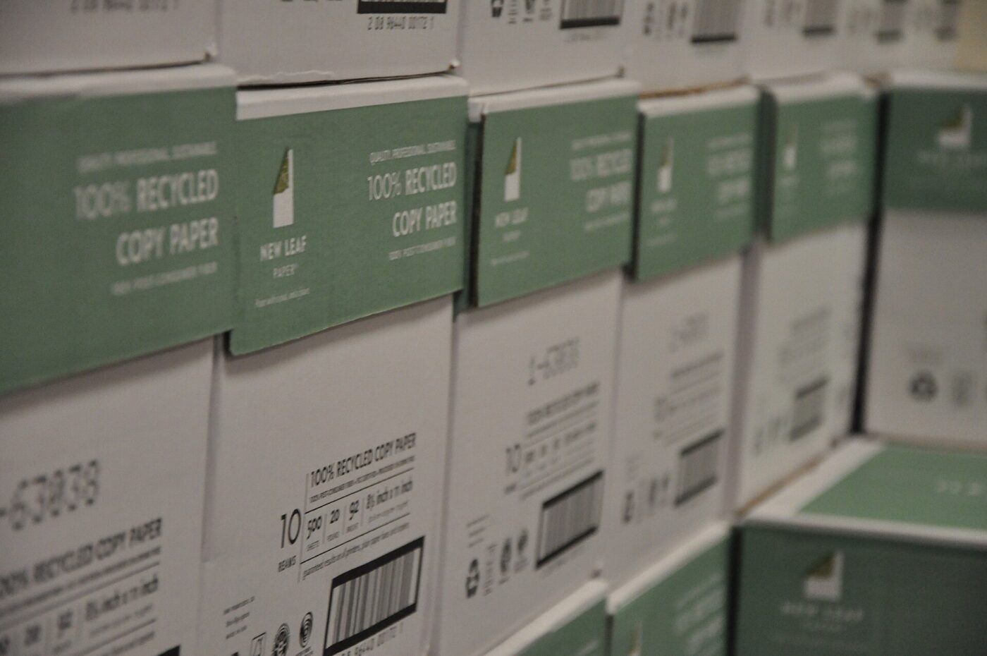 Cases of copy paper marked one hundred percent recycled, stacked in a supply room