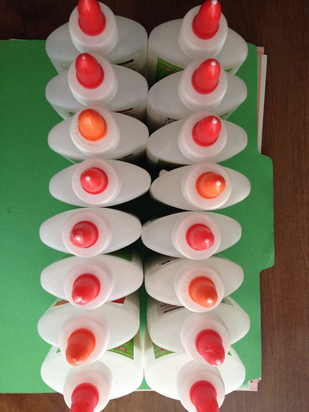 Rows of white craft glue bottles with red applicator caps laid on a folder.