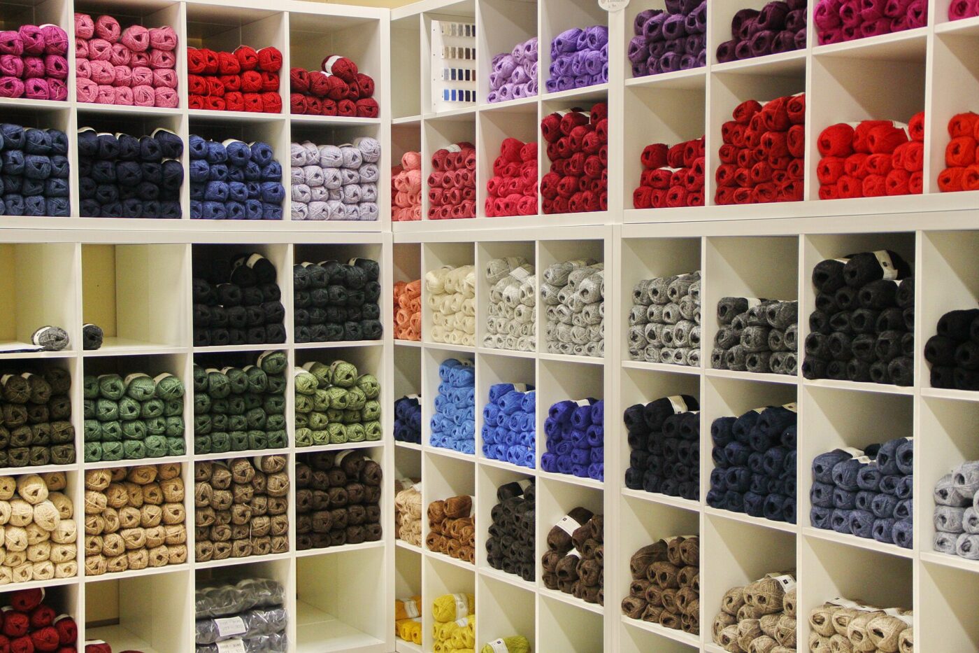 Rows of open cubbies filled with rolls of colored yarn and thread sorted by shade