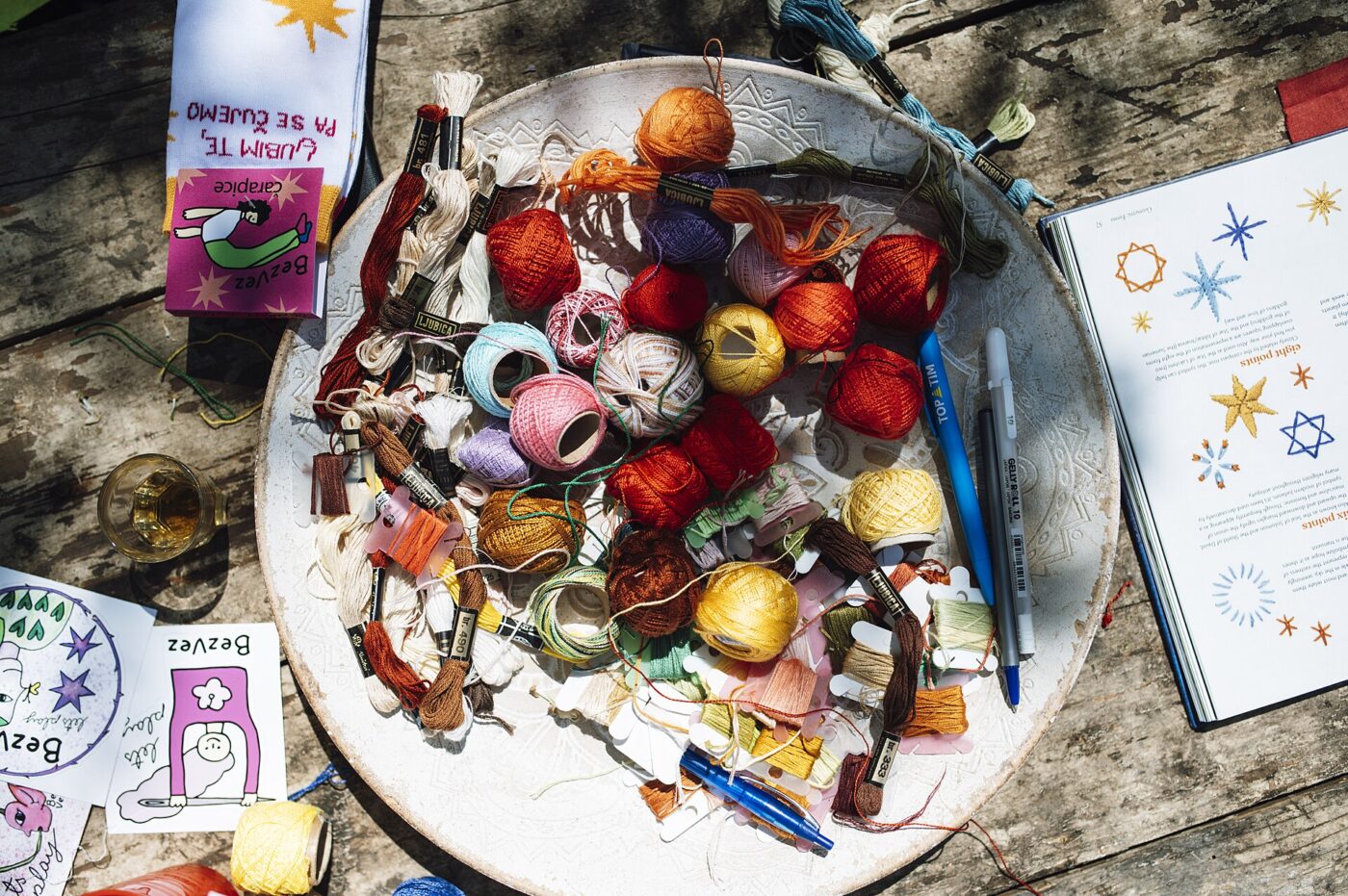 Yarn, embroidery floss and craft tools piled in a bowl on a weathered table.