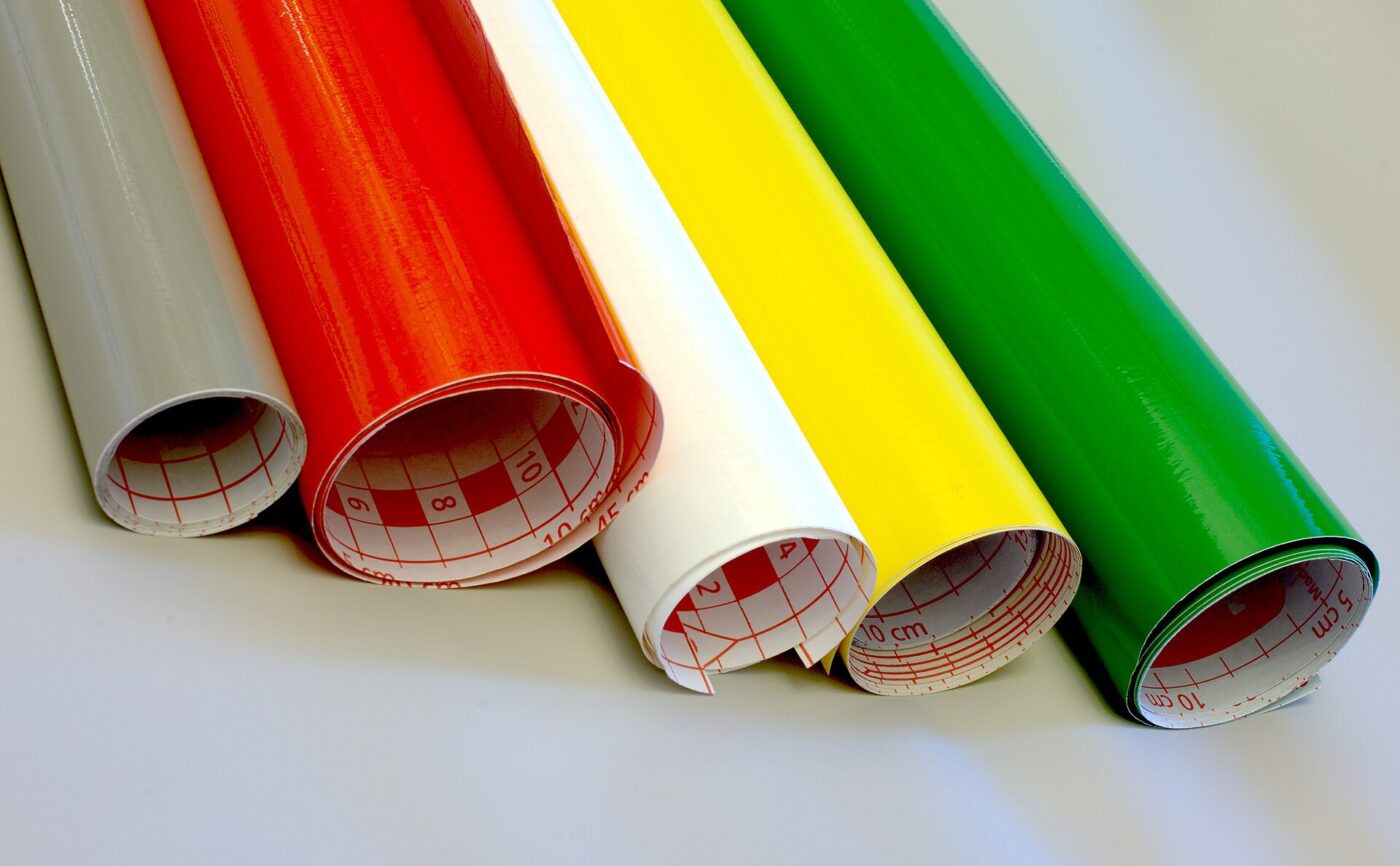 Rolls of colored self-adhesive vinyl film standing upright, gridded backing paper visible at the ends