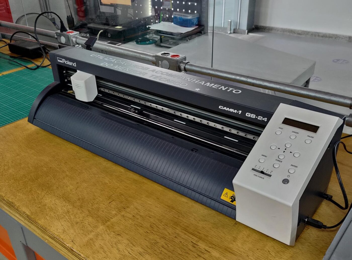 A desktop vinyl cutting plotter on a workbench, blade carriage parked over the roller.