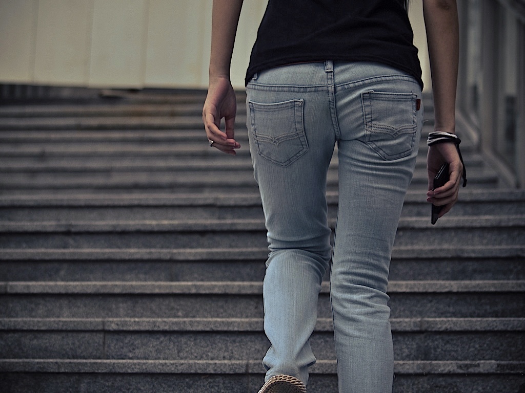 A person climbs concrete steps in light-wash jeans and sneakers, seen from behind