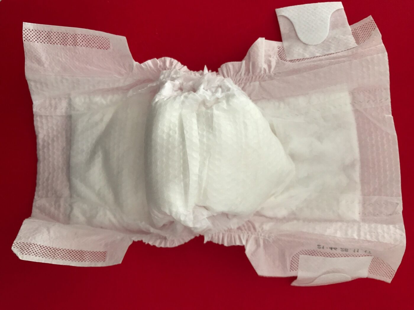An unfolded disposable baby diaper laid flat on a red surface, inner side up.