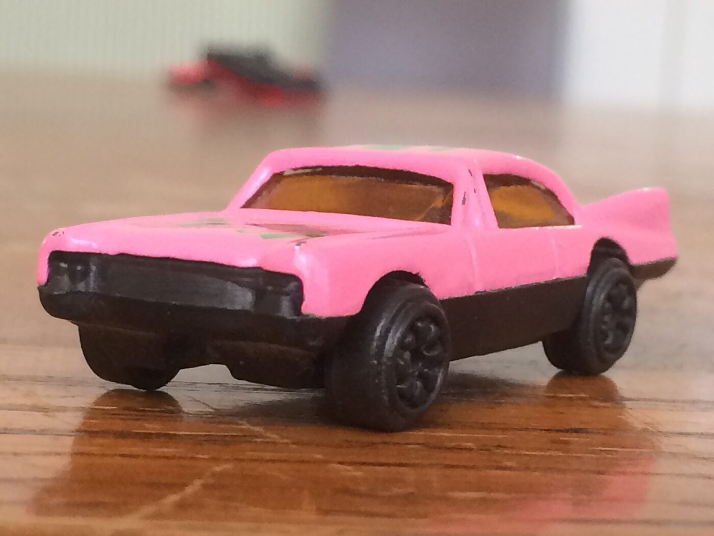 A small pink die-cast toy car photographed on a wooden tabletop.