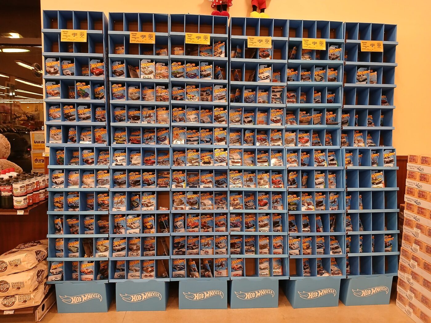 A store display wall of packaged die-cast toy cars in blue bins with price tags.