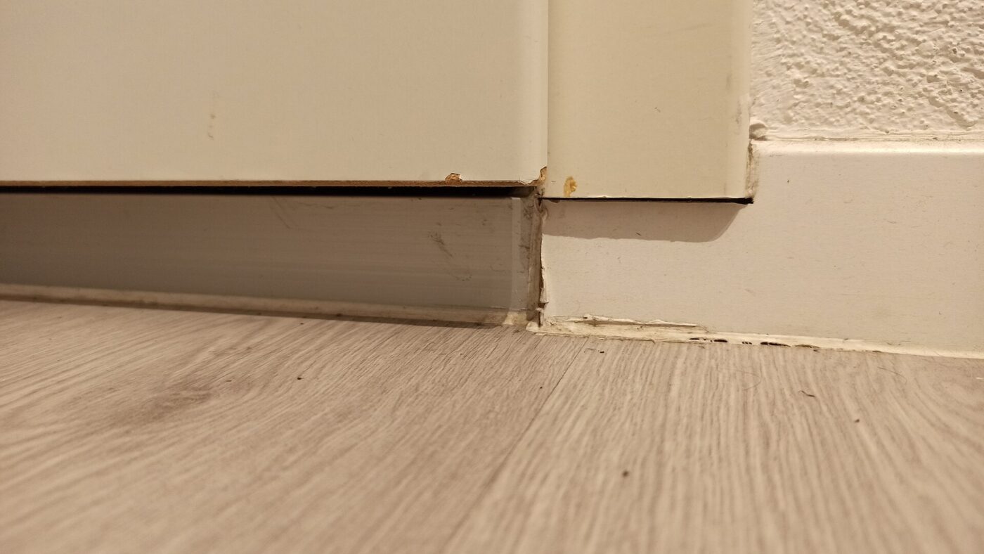 The bottom corner of a door, where the gap under it meets the frame and the floor.
