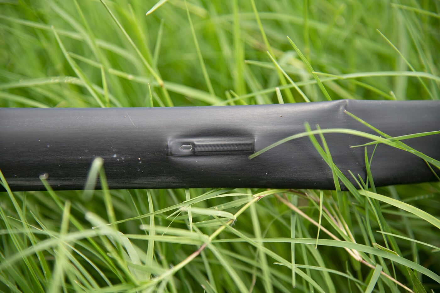 A black drip irrigation line lying in grass with an outlet slot in the tubing.