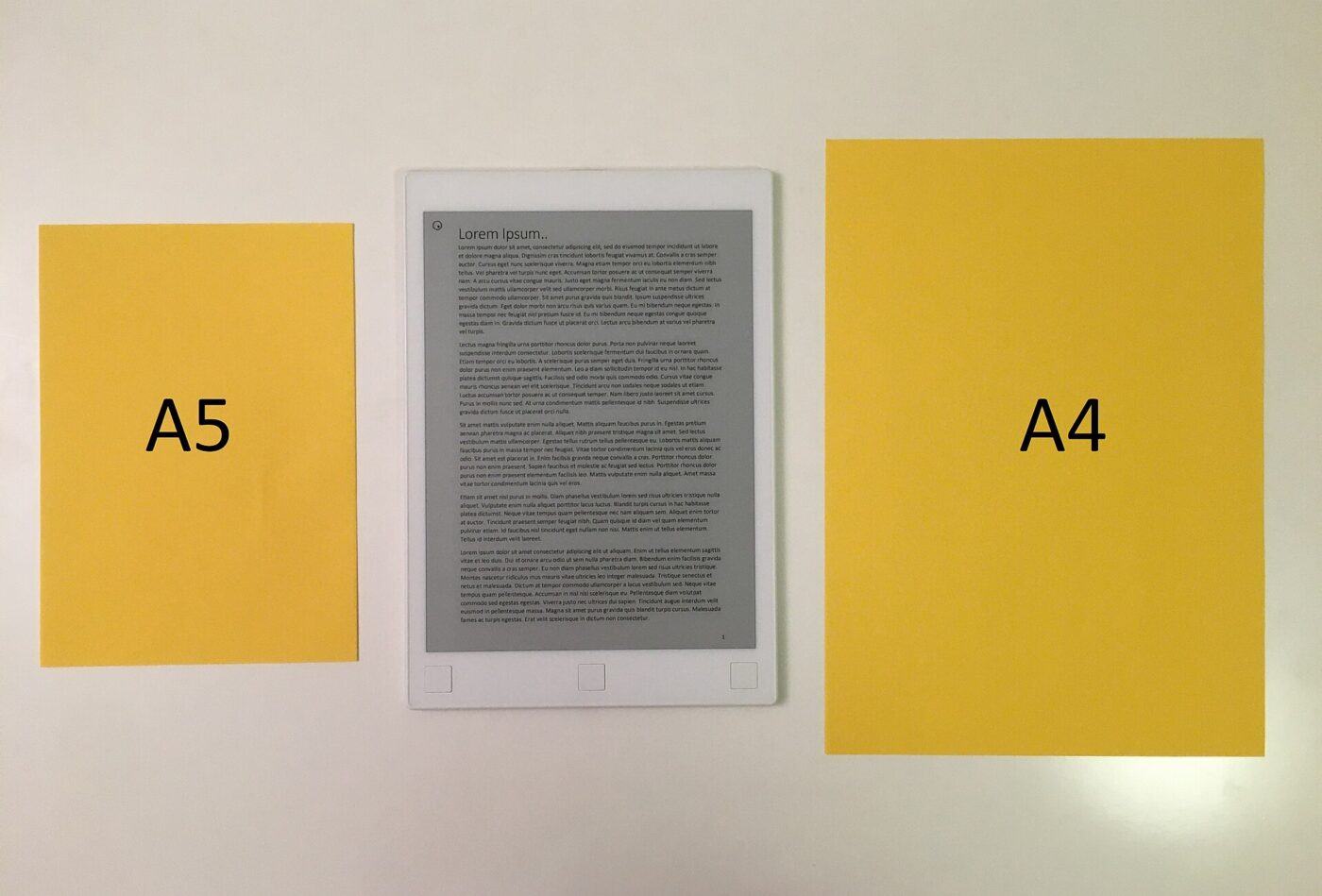 An e-paper writing tablet displaying text, laid between A5 and A4 sheets of paper for size