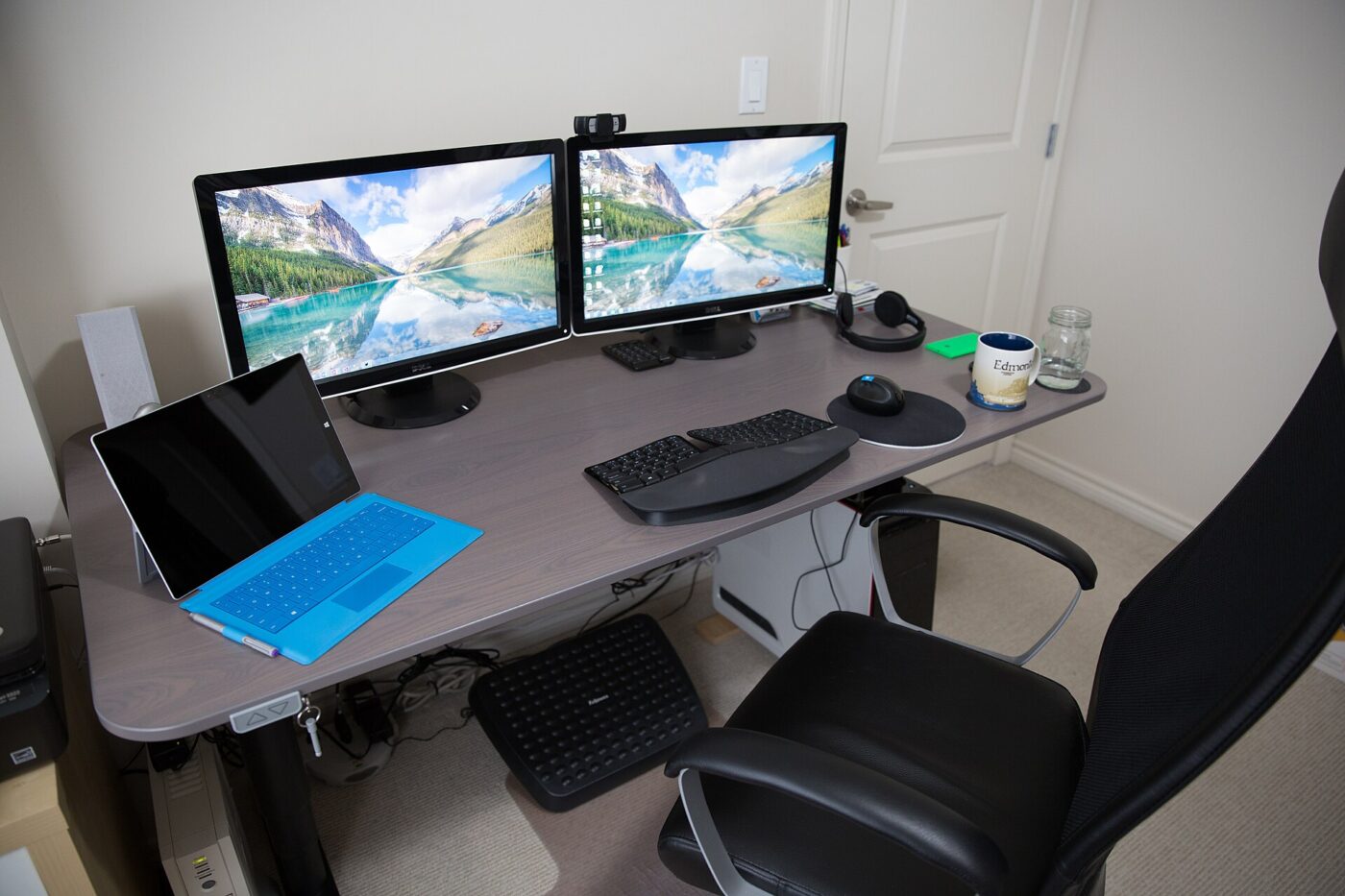 A height-adjustable desk at seated height, with two monitors, a keyboard and an office chair.