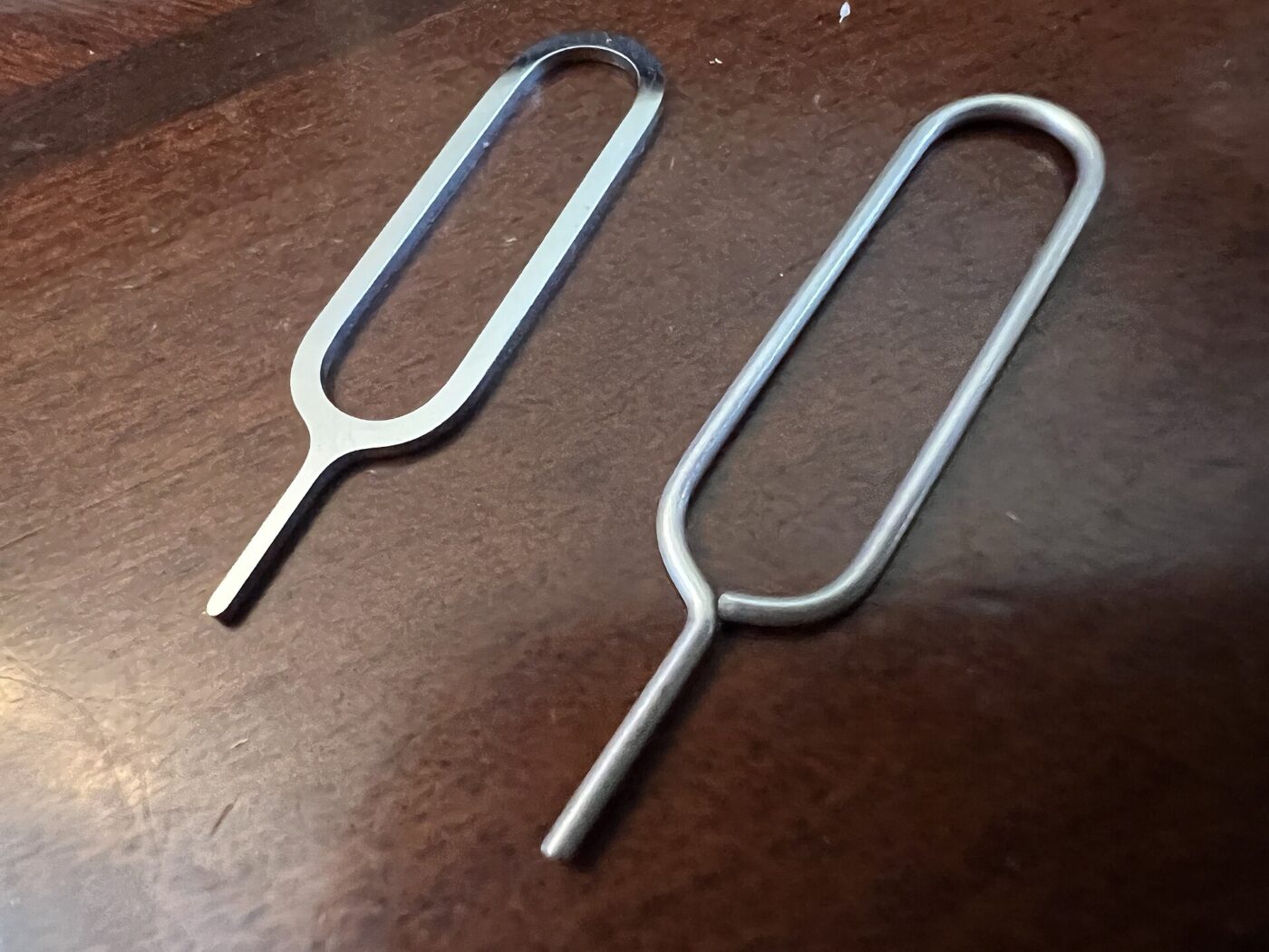 Two metal SIM tray eject pins lying on a wooden table.