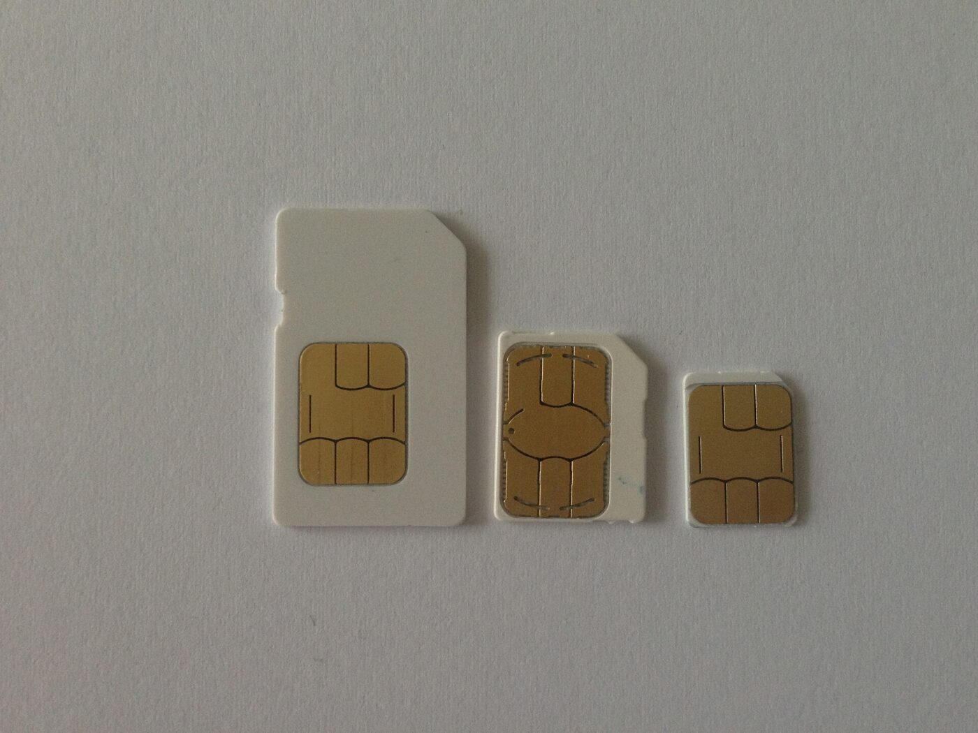 Mini, micro and nano SIM cards lined up by size on a plain surface.