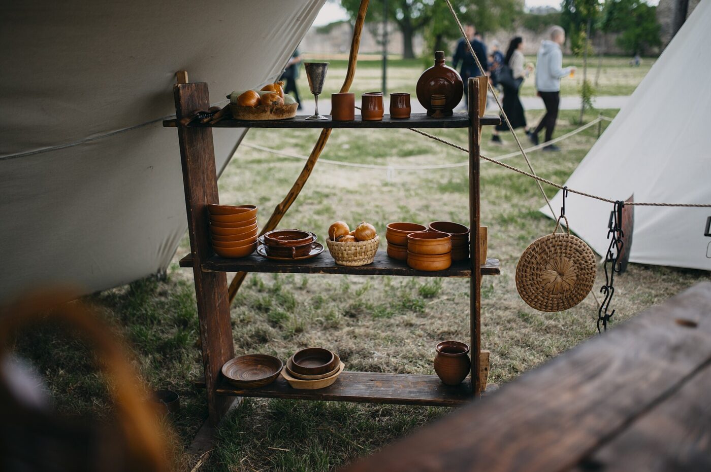 Clay cups, bowls and jugs displayed on a wooden shelf at an outdoor craft market