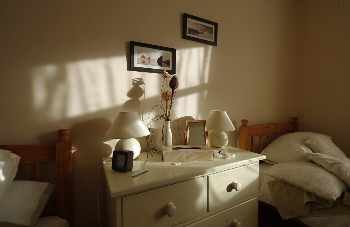 A painted chest of drawers standing beside a bed in a sunlit bedroom